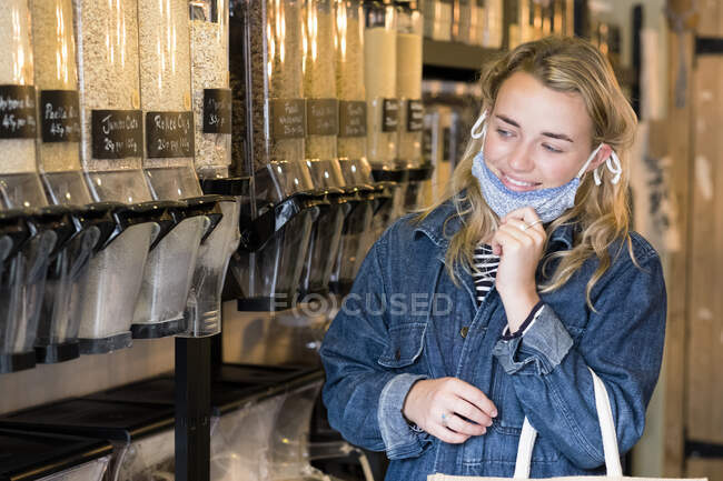 Junge blonde Frau mit Gesichtsmaske shoppt in abfallfreiem Vollwertladen. — Stockfoto