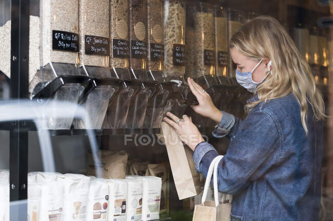 Giovane donna bionda con maschera viso, shopping in deposito di cibo intero senza rifiuti. — Foto stock