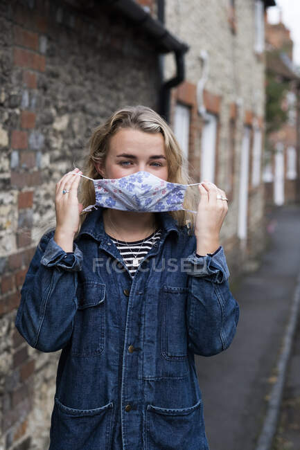 Jovem loira de pé ao ar livre, colocando em máscara facial. — Fotografia de Stock