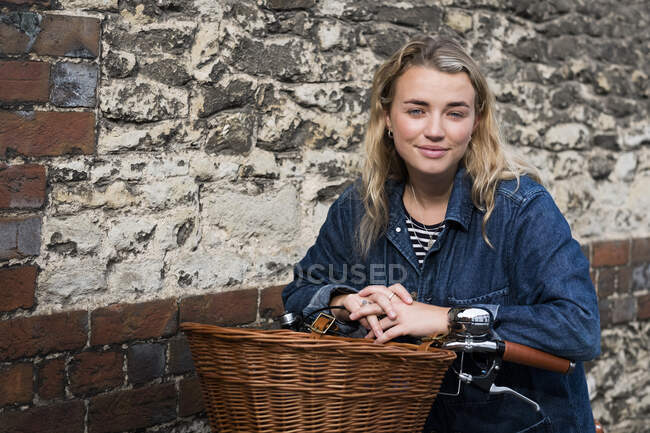 Mujer rubia joven en bicicleta con cesta, mirando a la cámara. - foto de stock
