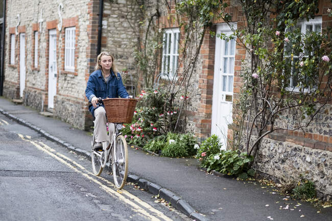 Joven mujer rubia en bicicleta por una calle del pueblo. - foto de stock