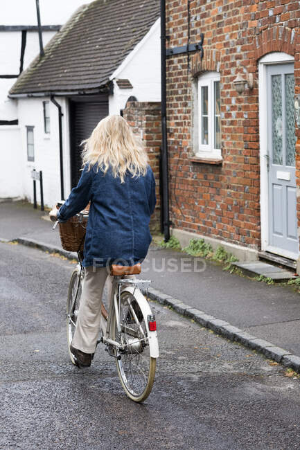 Visão traseira da jovem loira pedalando por uma rua da aldeia. — Fotografia de Stock