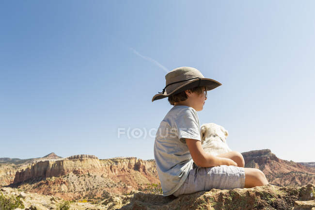 Молодий хлопчик сидить на камені зі своїм собакою — стокове фото