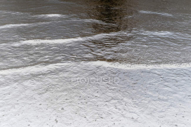 Detalle de ondas oceánicas ligeras y ondulaciones sobre arena, imagen invertida. - foto de stock