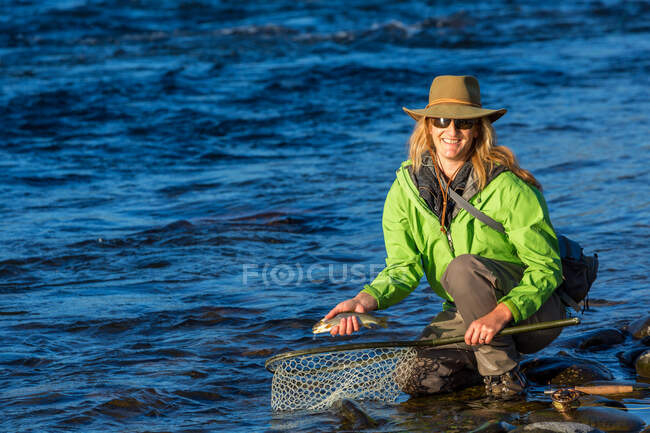 Fliegenfischerin landet Forelle mit Netz auf Fluss, Britisch-Kolumbien, Kanada. — Stockfoto