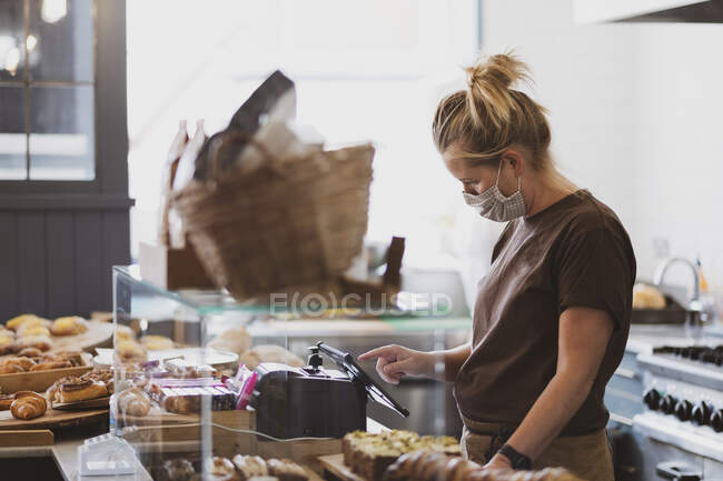 Serveuse blonde portant un masque facial travaillant dans un café. — Photo de stock
