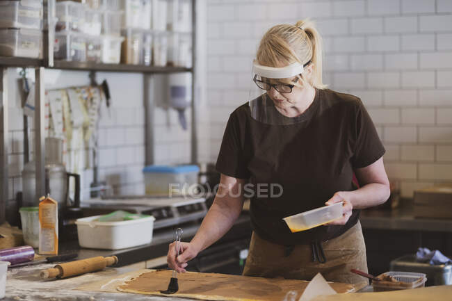 Blonde Kellnerin mit Mundschutz arbeitet in einem Café und bereitet Essen zu. — Stockfoto
