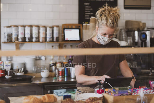Camarera rubia con máscara facial trabajando en un café. - foto de stock