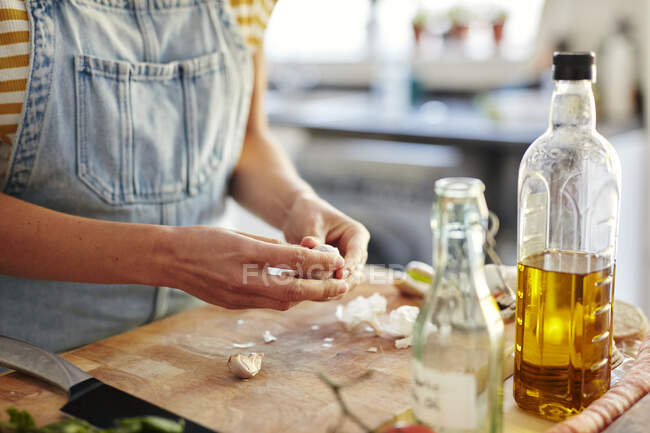 Woman in kitchen preparing garlic for cooking on chopping board — Stock Photo