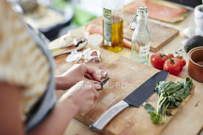 Woman in kitchen preparing garlic for cooking on chopping board — Stock Photo