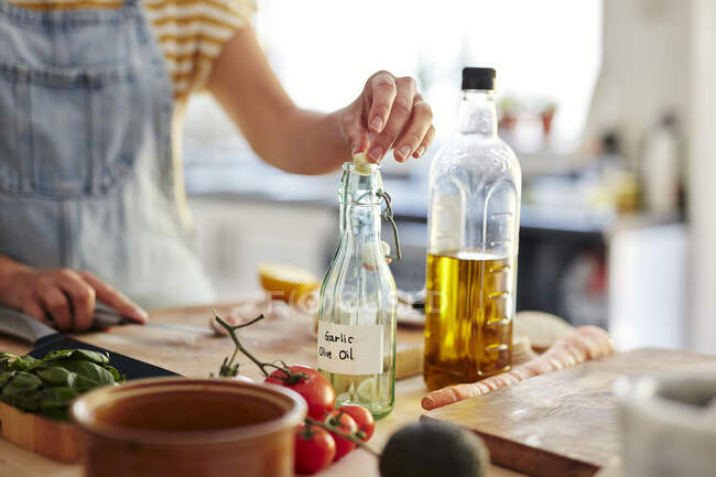 Woman putting garlic into bottle of olive oil in kitchen — Stock Photo