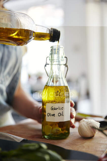 Femme versant de l'huile d'olive dans une bouteille contenant de l'ail — Photo de stock