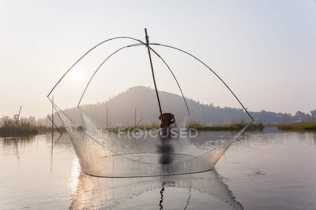Pescador em seu barco movendo redes de balanço arqueadas acima da água no Lago Loktak — Fotografia de Stock