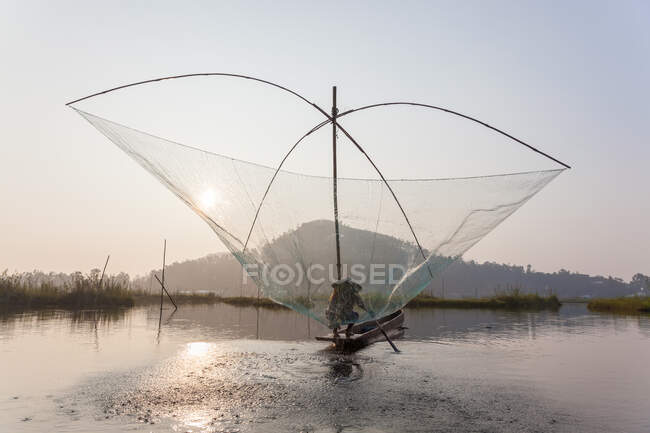 Pescador em seu barco movendo redes de balanço arqueadas acima da água no Lago Loktak — Fotografia de Stock