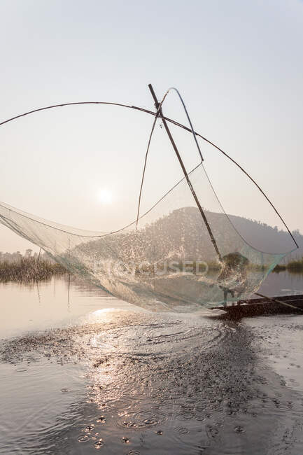 Fisherman on his boat moving arched swing nets above the water at  Loktak Lake — Stock Photo