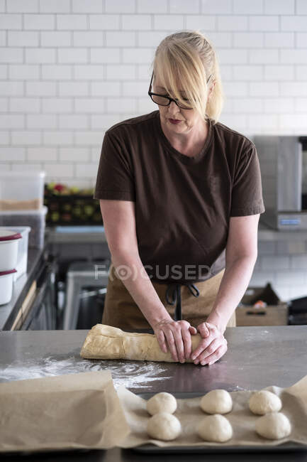 Женщина в коричневом фартуке, стоящая на кухне кафе, смешивая выпечку из теста — стоковое фото