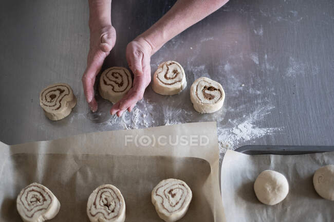 High angle close up of person shaping dough for Cinnamon Rolls on metal surface. — Stock Photo