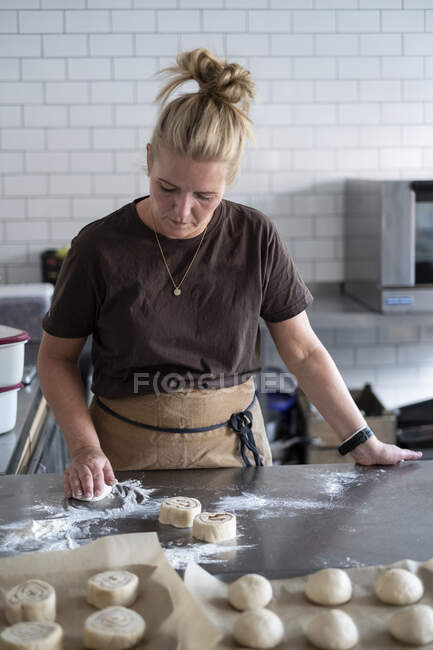 Femme blonde portant tablier marron debout dans une cuisine, pâtisserie danoise. — Photo de stock