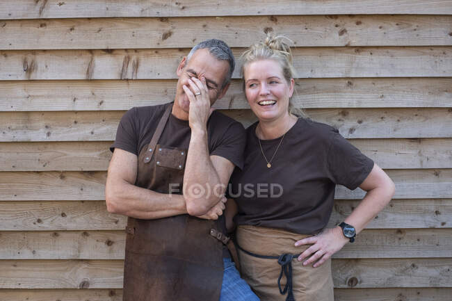 Hombre y mujer en delantales, colegas tomando un descanso del trabajo, riendo - foto de stock