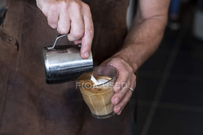 Close up of barista wearing brown apron pouring cafe latte. — Stock Photo