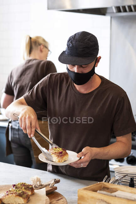 Homme barista portant casquette de baseball noire et masque facial travaillant derrière le comptoir. — Photo de stock