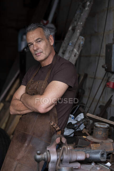 Portrait de barista mâle aux cheveux gris courts, portant un tablier marron, les bras croisés, regardant la caméra. — Photo de stock