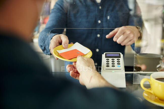 Homem entregando cartão de crédito e conta para garçom atrás da tela de plástico no café — Fotografia de Stock