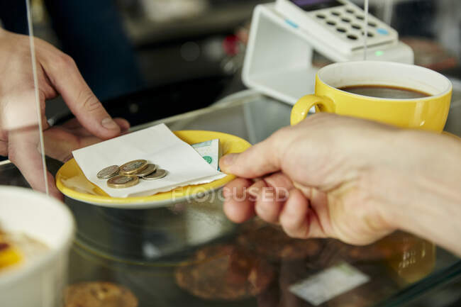 Close up of hands exchanging plate with money for payment in cafe — Stock Photo