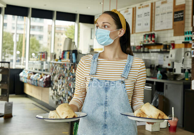 Официантка в маске с двумя тарелками еды для клиентов — стоковое фото