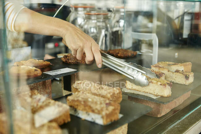 Primer plano de pinzas seleccionando una rebanada de pastel en la cafetería - foto de stock