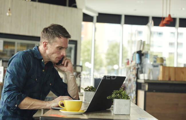 Hombre sentado en un café, trabajando en un portátil - foto de stock