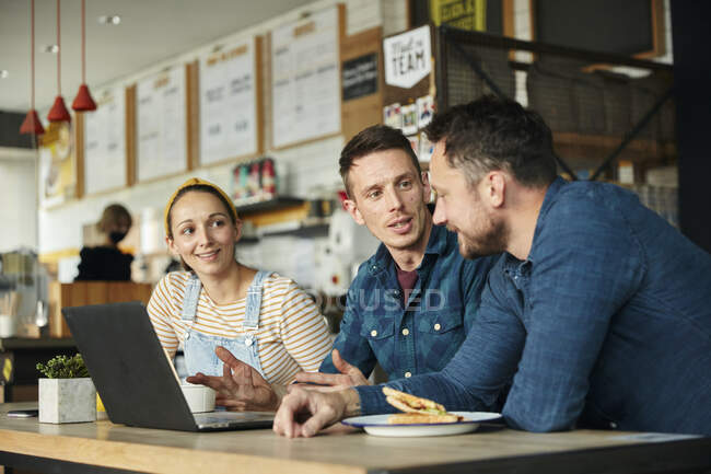 Two men and a woman meeting in a cafe, looking at a laptop — Stock Photo