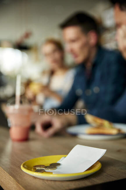 Menschen an einem Cafétisch, eine Untertasse mit Kassenbon und Barzahlung — Stockfoto