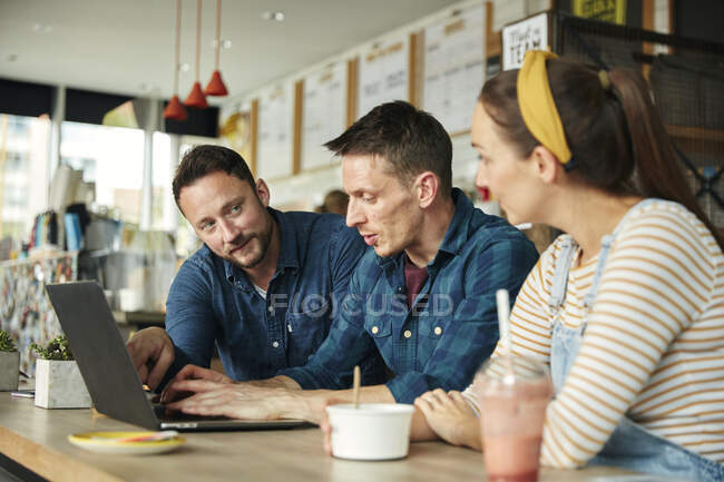 Dos hombres y una mujer reunidos en un café, mirando un portátil - foto de stock