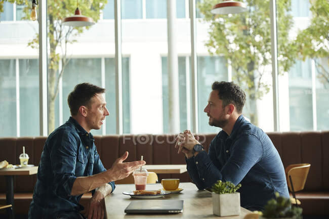 Deux hommes assis dans un café discutant, ayant une réunion. — Photo de stock