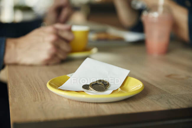 Kleine Untertasse mit Kassenbon und Münzen, Bargeld auf einem Cafétisch. — Stockfoto