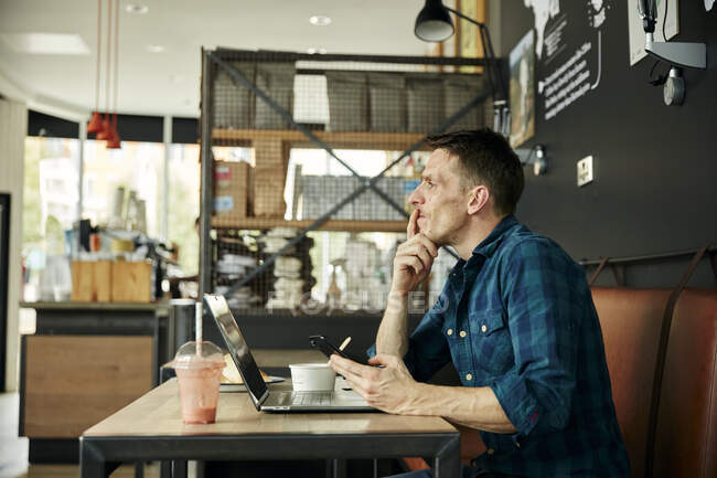 Uomo seduto in un caffè con un computer portatile, indossando le cuffie, prendendo una chiamata online. — Foto stock