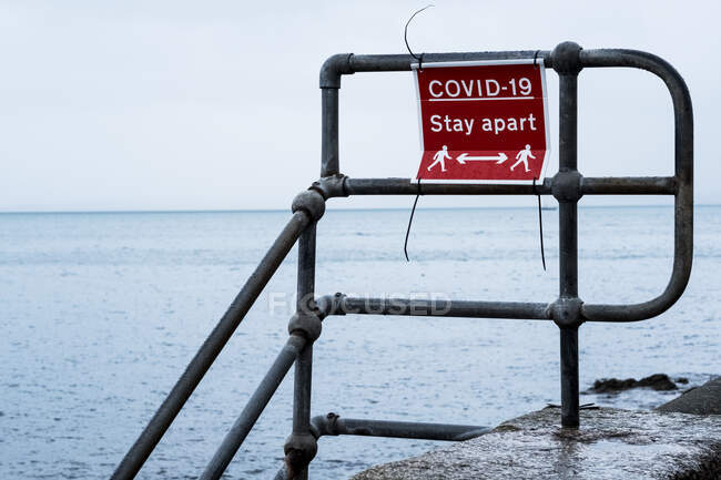 Rot-weißes Distanzschild Covid-19 an einem Geländer der Hafenmauer. — Stockfoto