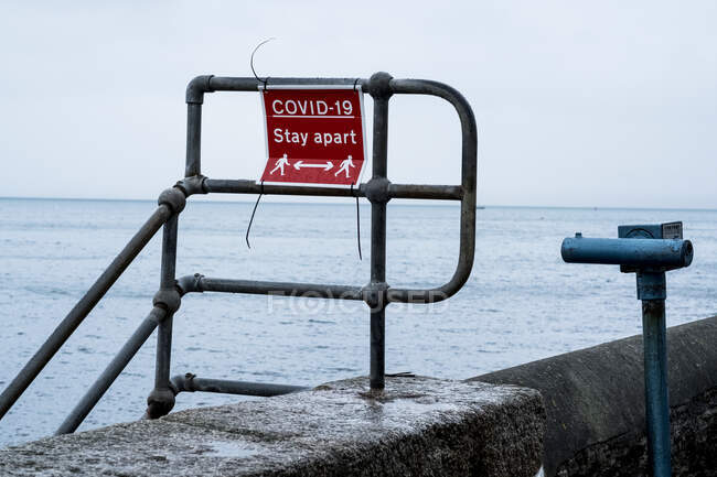 Red and white Covid-19 distancing sign on a harbour wall railing. — Stock Photo