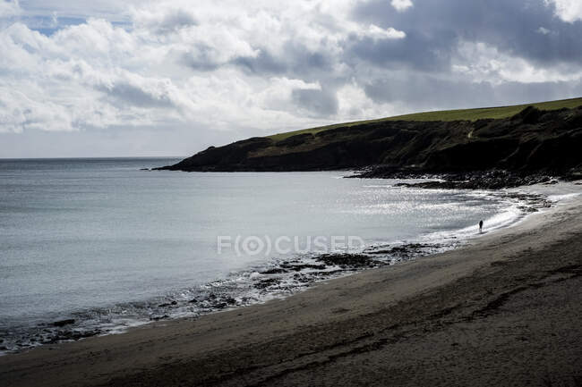 View along a sandy beach with distant cliff under a cloudy sky. — Stock Photo