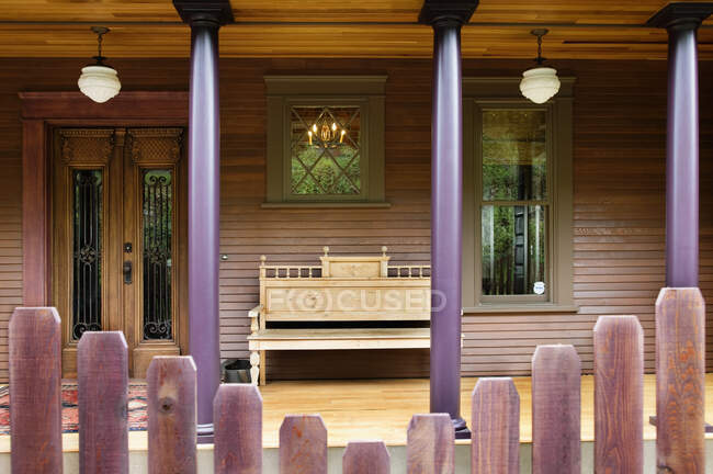 Valla de madera y porche de casa con columnas y banco. - foto de stock