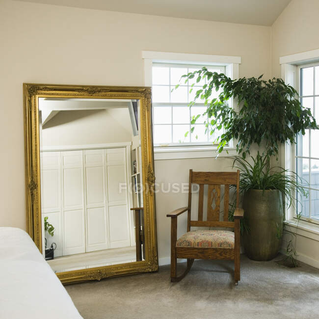 Gold mirrror and rocking chair with potted plant in bedroom. — Stock Photo