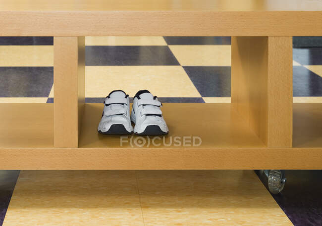 Pair of child trainers in rolling storage crate on tiled floor. — Stock Photo