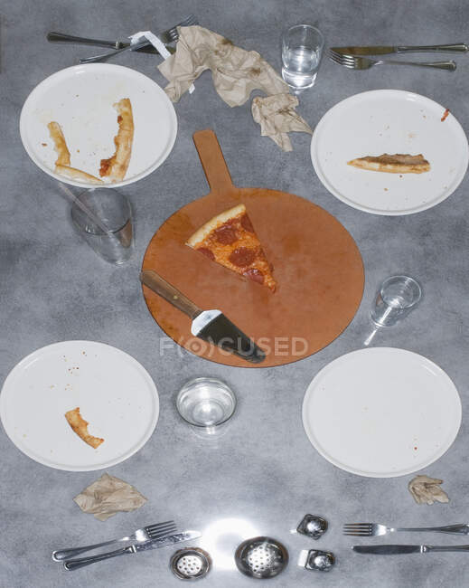 Restos de una comida de pizza con sobras de rebanada y costras, vasos y platos y servilletas. - foto de stock