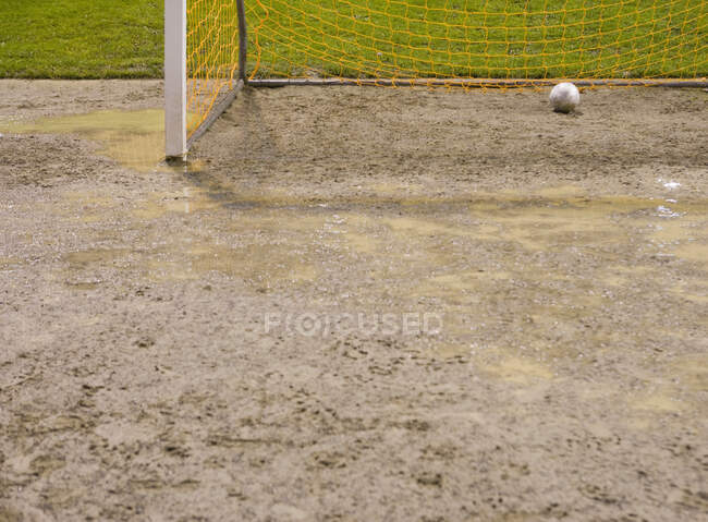 Ballon de football dans le filet de but sur le terrain de football boueux. — Photo de stock