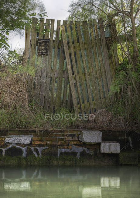 Dilapidated wooden fence on canal waterfront. — Stock Photo