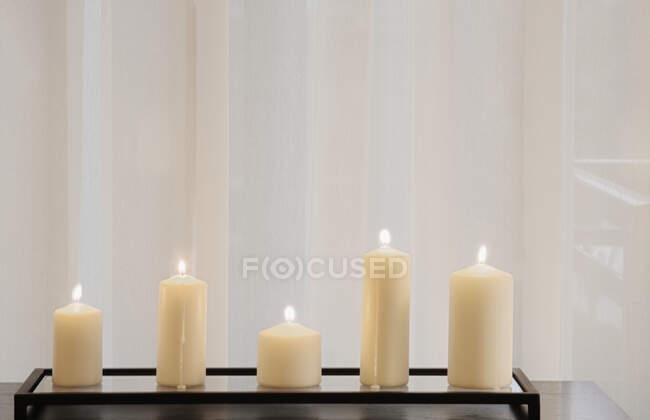 Pillar candles lit and lined up in front of curtain — Stock Photo