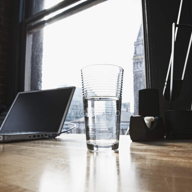 Ordinateur portable et verre d'eau potable sur le bureau dans les bureaux urbains — Photo de stock