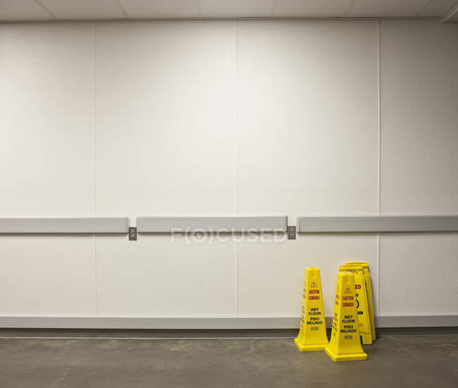 Coni di avvertimento a pavimento bagnato con parete bianca dietro — Foto stock