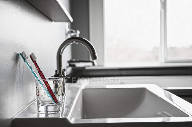 Escovas de dentes em beber vidro no banheiro doméstico. — Fotografia de Stock